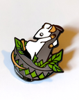 Photo. A smooth enamel pin badge, of a stylised cartoon mouse standing in a mortar and pestle, grinding leaves.