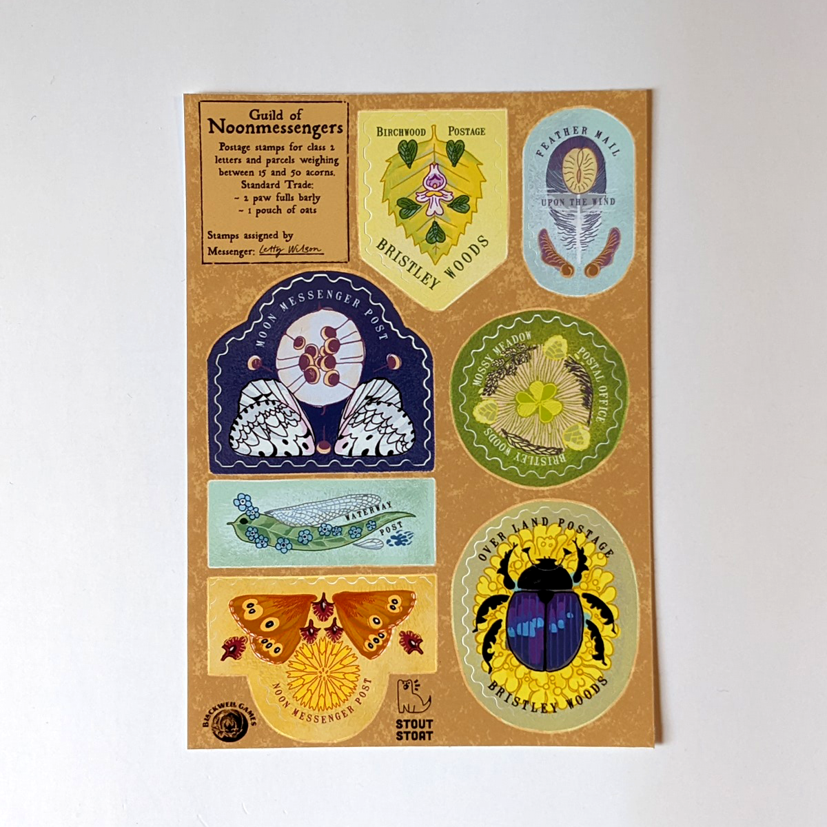 Photo. A sticker sheet from the Apawthecaria Deluxa bundle. There are 7 differently shaped stamps with die-cut franking around their edges, so that each stamp peels to look like a realistic stamp. The stamps feature natural elements, like moth wings and pressed flowers, as if they were made by animals for a beastly postal service.