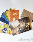 Photo. The deluxe set for Apawthecaria, showing 5 illustrated post cards, a sticker sheet of stamp designs, and a pin badge of a potion-making mouse, alongside the book Apawthecaria and its game map.